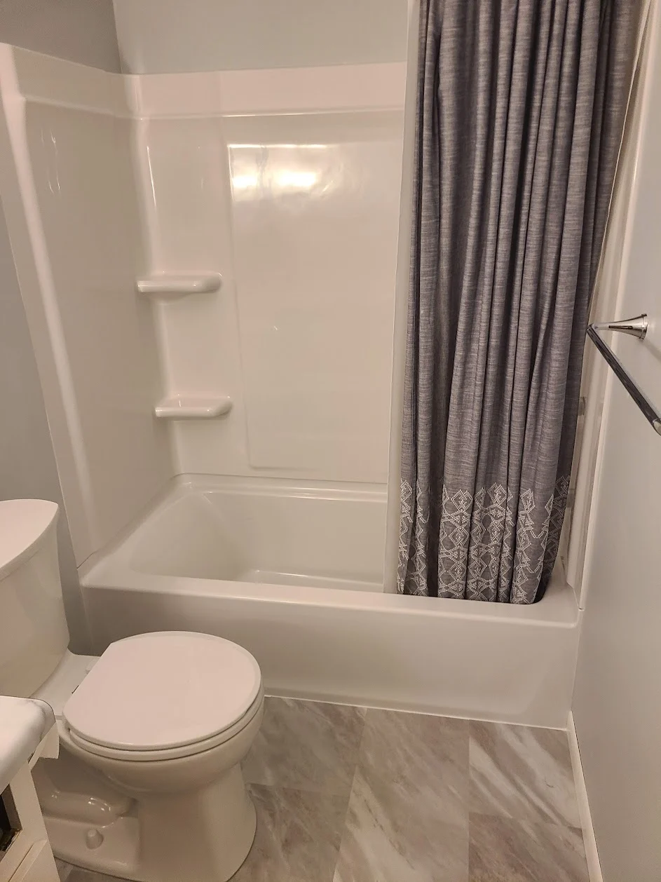 White tub and shower surround with luxury vinyl flooring in an economy bathroom